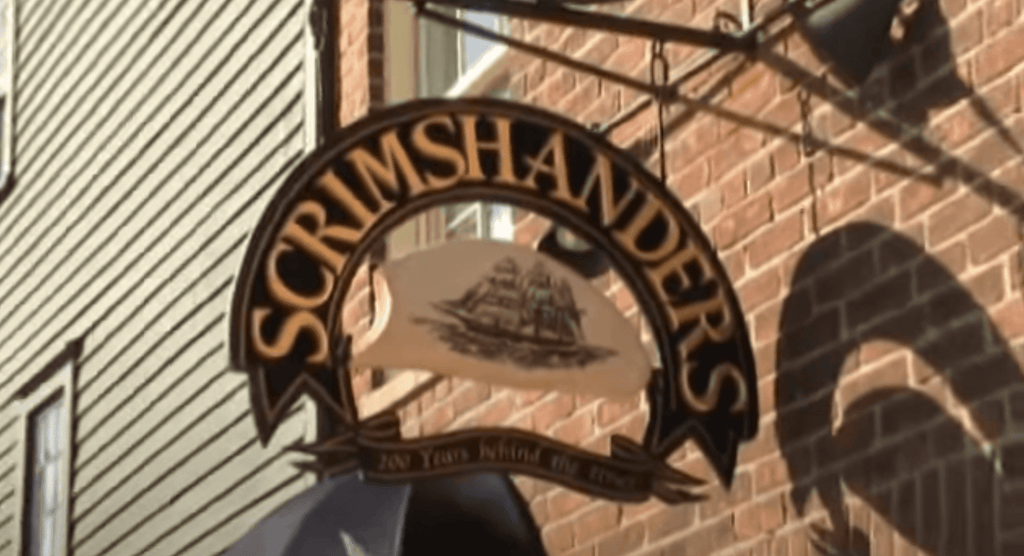 Scrimshanders building sign hanging from brick wall.